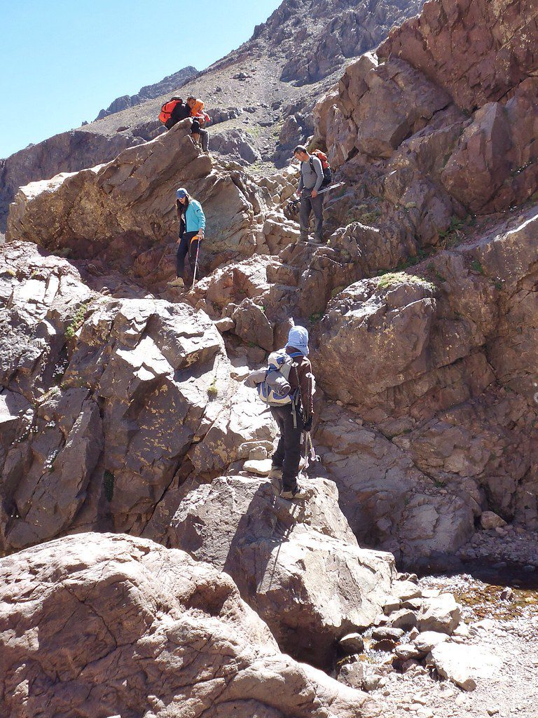 Climbers ascending the rugged slopes of Mount Toubkal, surrounded by the majestic High Atlas mountains under a clear blue sky