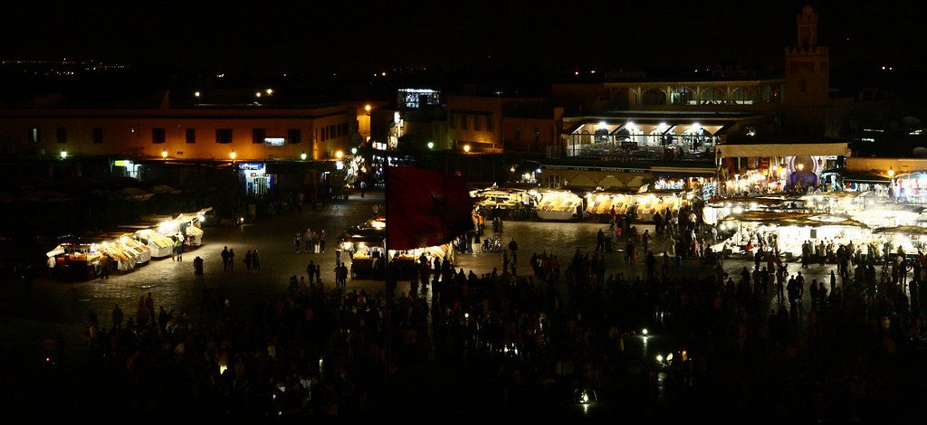 Vibrant view of the bustling Jemaa el-Fnaa square in Marrakech, showcasing street performers, food stalls, and the Koutoubia Mosque in the background during sunset