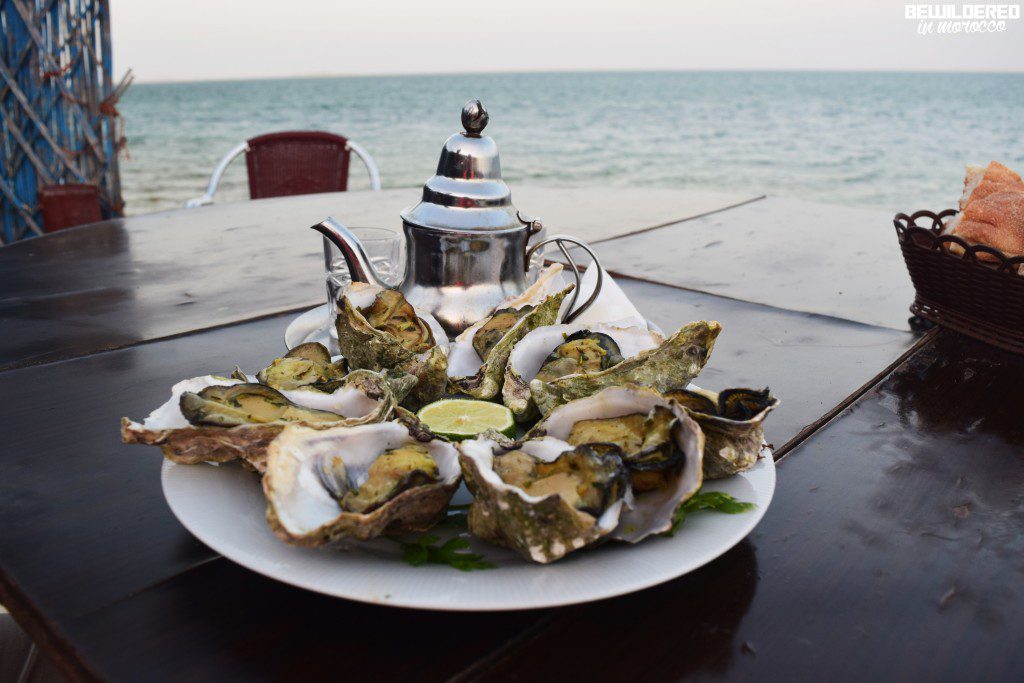 An assortment of fresh seafood displayed at a market in Dakhla City, featuring a variety of fish, shellfish, and crustaceans. Vibrant colors and textures highlight the local fishing culture, with the picturesque coastal backdrop of Dakhla in the background.