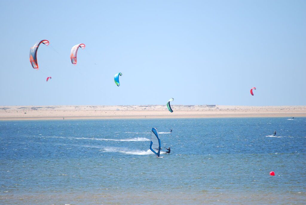 Surfers riding the waves in Dakhla, Morocco, with stunning coastal scenery and clear blue skies.