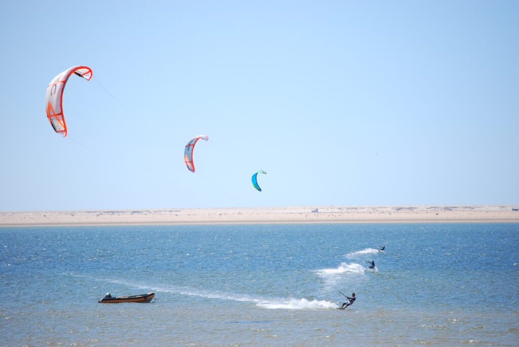 Thrilling scene of kitesurfers gliding across the turquoise waters of Dakhla City, with colorful kites soaring high against a backdrop of clear blue skies. The sandy beaches and rugged coastline of Dakhla create a picturesque setting for this popular water sport.