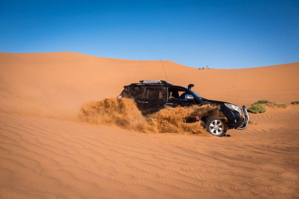 4x4 vehicle driving through the sandy desert dunes in Zagora, Morocco, with mountains in the distance