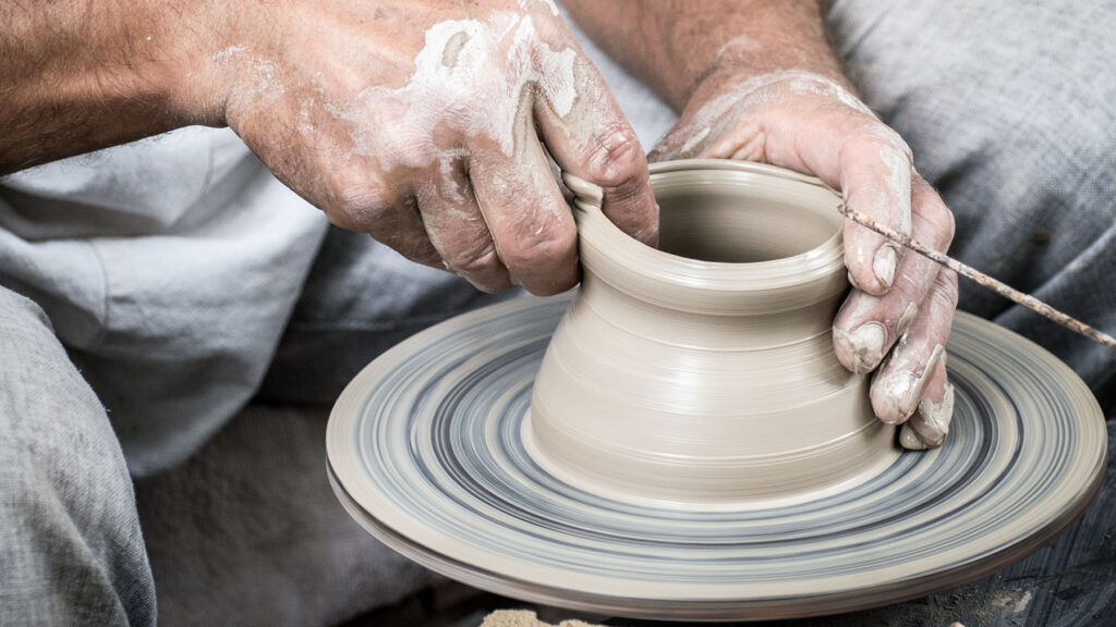 Artisan shaping traditional Moroccan tajines and various clay tools, surrounded by pottery and crafting tools in a workshop. The image showcases the intricate details and craftsmanship involved in creating these iconic Moroccan cooking vessels